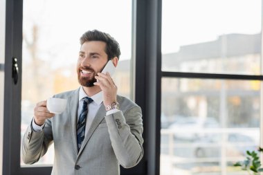 Gülümseyen işadamı cep telefonuyla konuşuyor ve elinde fincanı tutuyor. 