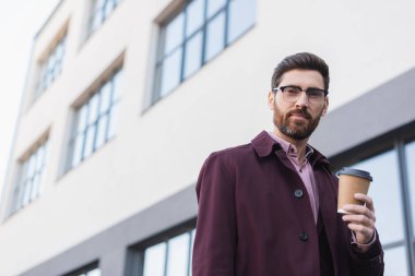 Trençkotlu sakallı iş adamının şehir sokaklarında kahve içmesi düşük bir açı. 