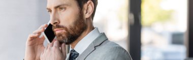 Dalgın takım elbiseli işadamı ofiste akıllı telefondan konuşuyor. 