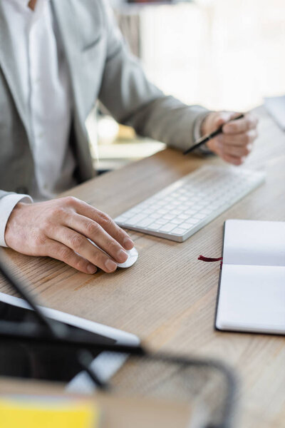 Cropped view of businessman using computer mouse near notebook in office 