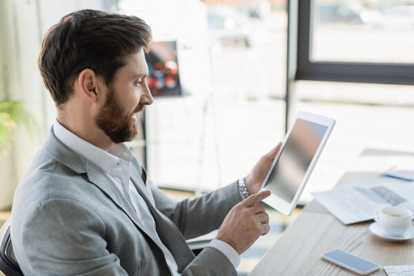 Side view of smiling businessman pointing at digital tablet in office 
