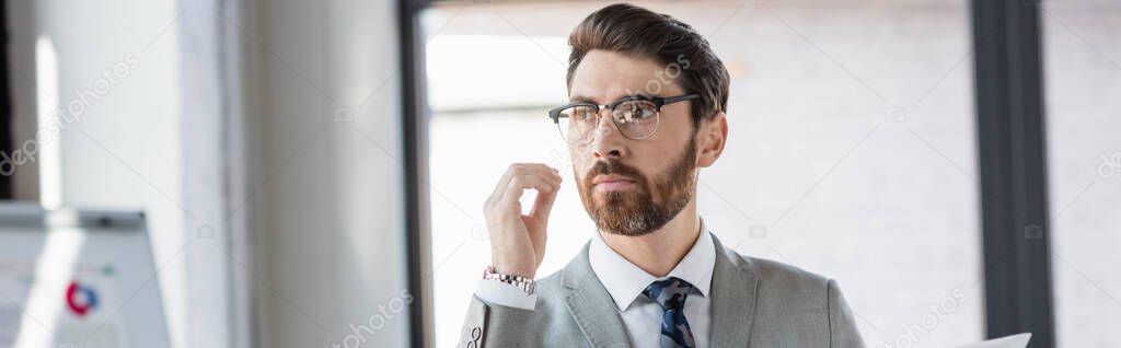 Bearded businessman in eyeglasses and suit standing in office, banner 