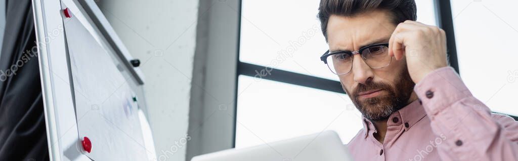 Focused businessman using digital tablet near flip chart in office, banner 