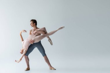 full length of shirtless man and sensual ballerina performing ballet dance on grey clipart