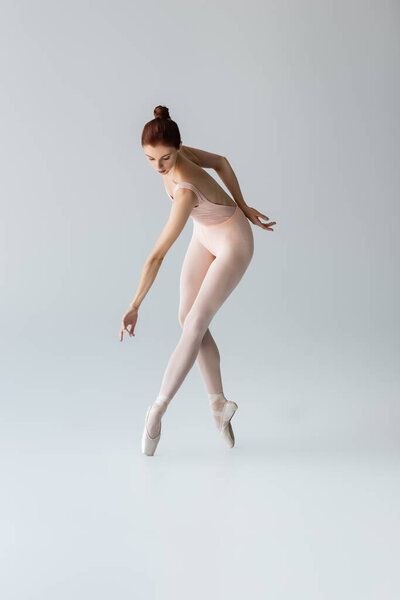 full length of sensual ballerina in pointe shoes and bodysuit dancing on gray
