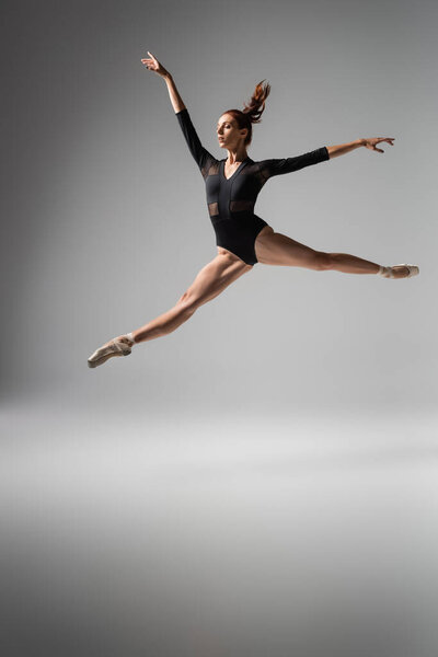 Легкая балерина в пуантах и черных ботинках прыгает на темно-сером
