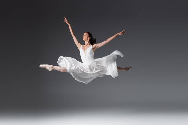 Полная длина изящной женщины в белом платье, прыгающей на темно-сером