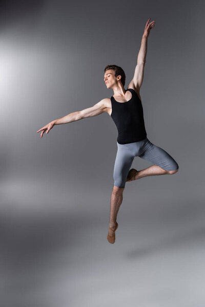 молодая и грациозная артистка балета жестикулирует, левитируя на темно-сером