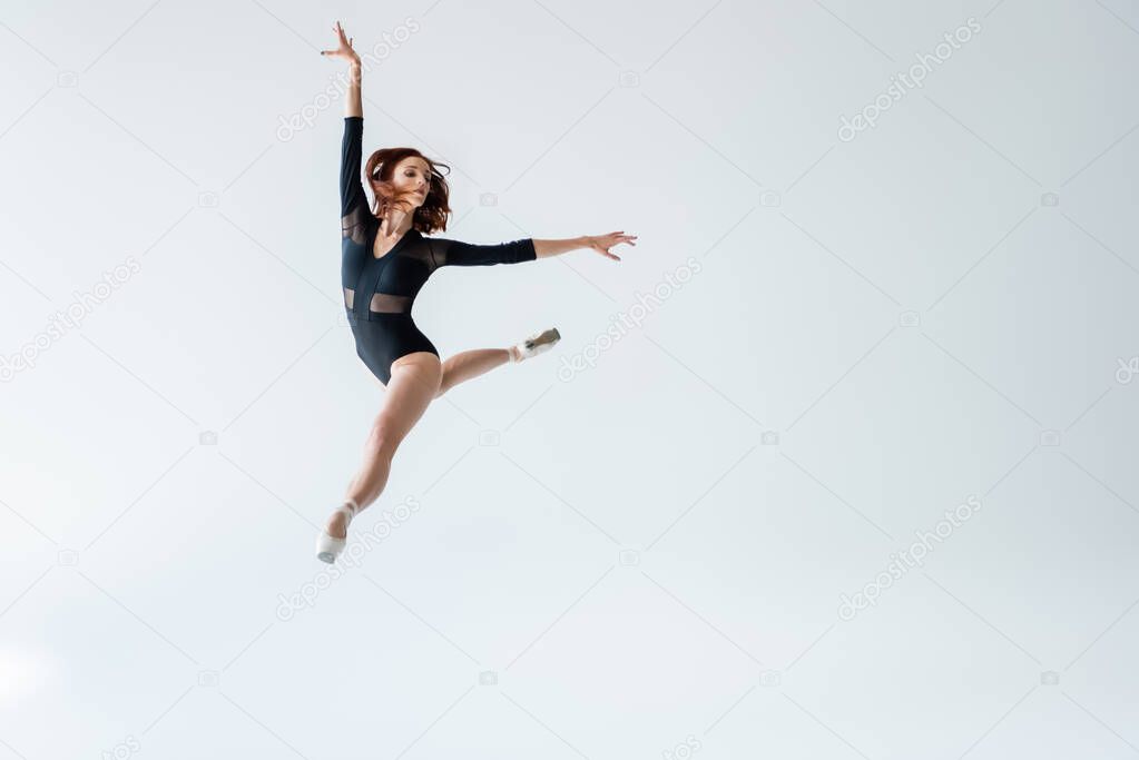 full length of ballerina in black bodysuit jumping isolated on gray