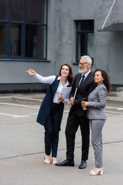 Gülümseyen etnik çeşitlilikteki iş adamları dışarıyı gösteren emlak komisyoncusunun yakınına bakmıyorlar.