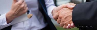 partial view of businessman shaking hands with blurred realtor with digital tablet and key outdoors, banner clipart