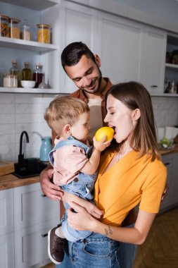 Küçük çocuk evde anne ve babasının yanında limon tutuyor. 