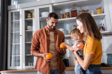 Baba evde oğluyla birlikte karısına portakal tutuyor. 