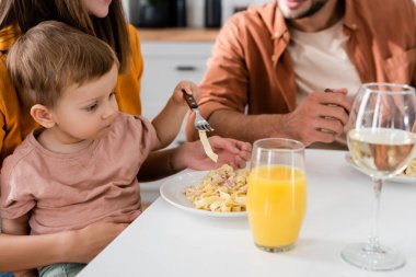 Küçük çocuk ailesinin yanında çatal ve mutfakta makarna tutuyor. 