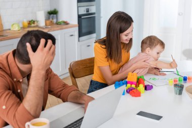 Gülümseyen anne ve babasının yanında oynayan çocuk evde dizüstü bilgisayar kullanıyor. 