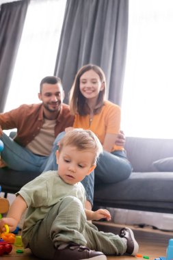 Küçük çocuk oturma odasındaki kanepede bulanık ebeveynlerin yanında oyun oynuyor. 