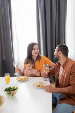 Evde yemek yerken kocasının ve oğlunun yanında şarap tutan neşeli bir kadın. 