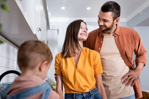 Sonrientes Padres Mirándose Cerca Niño Borroso Cocina —  Fotos de Stock