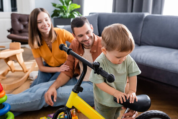 Toddler child standing near bike and parents at home 