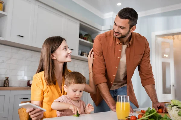 Mujer Feliz Sosteniendo Teléfono Inteligente Cerca Hijo Marido Cocina Ensalada — Foto de Stock