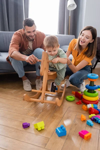 Padres Sosteniendo Hijo Pequeño Mecedora Cerca Juguetes Sala Estar —  Fotos de Stock