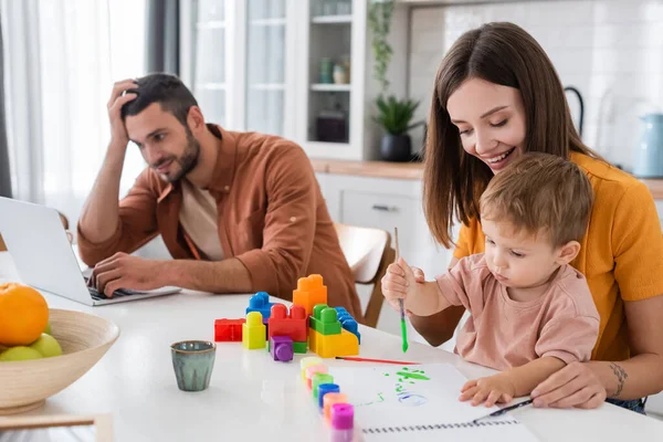 Young Woman Sitting Son Drawing Husband Using Laptop Home — Stock Photo, Image