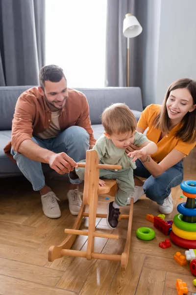 Glückliche Eltern Halten Kind Der Nähe Von Schaukelpferd Und Spielzeug — Stockfoto