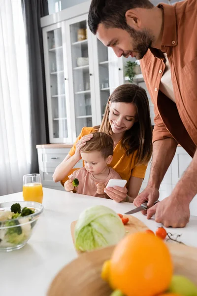 Leende Mamma Håller Smartphone Nära Son Och Make Matlagning Hemma — Stockfoto