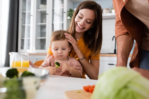 Ung Kvinna Kramar Son Håller Broccoli Nära Grönsaker Och Make — Stockfoto