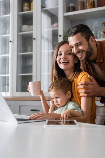 Homem Feliz Abraçando Esposa Com Copo Perto Filho Gadgets Casa — Fotografia de Stock