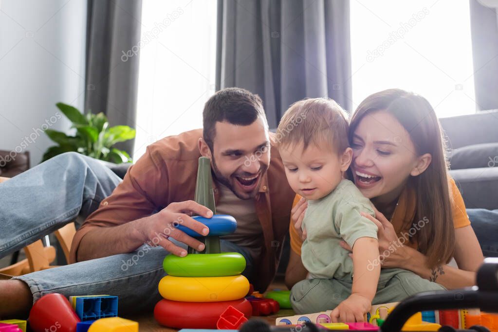 Happy parents hugging son near toys in living room 
