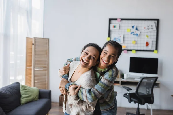 Alegre Afroamericana Mujer Con Hija Abrazando Mientras Mira Cámara Cerca — Foto de Stock