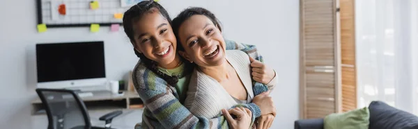兴奋的非洲裔美国人母亲和女儿一边在家里拥抱一边看着相机 高举横幅 — 图库照片