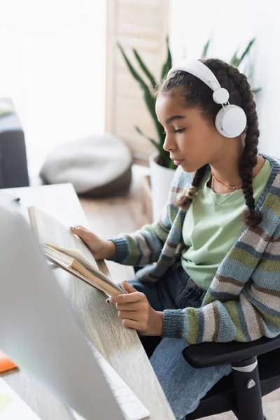 African American Schoolgirl Headphones Reading Book Blurred Computer Monitor — Stock Photo, Image