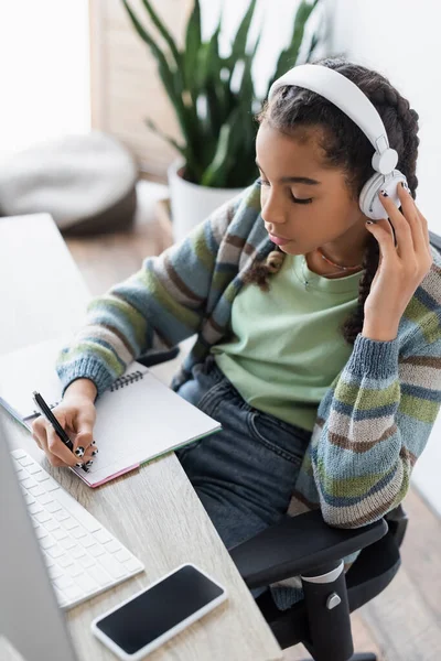 Adolescente Afroamericano Escribiendo Cuaderno Mientras Escucha Una Lección Audio Auriculares — Foto de Stock