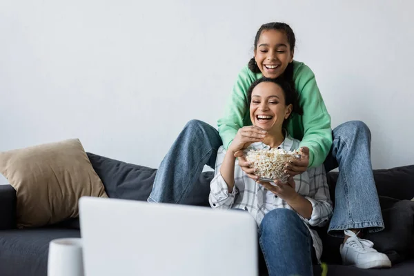 快乐的非洲裔美国女人 带着十几岁的女儿在笔记本电脑上看电影 旁边是一碗爆米花 — 图库照片