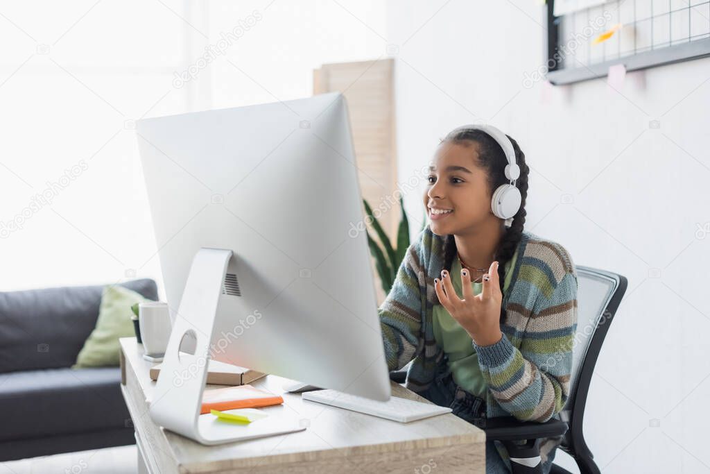 cheerful african american girl in headphones gesturing near computer at home