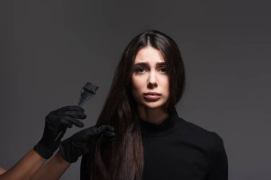 Kahverengi saçlı, koyu gri saçlı, üzgün bir kadının yanında saç fırçası tutan kuaför.