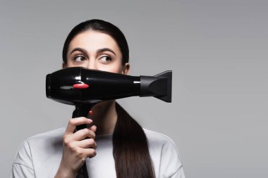 Gri tişörtlü, yüzü saç kurutma makinesiyle kaplı genç bir kadın.