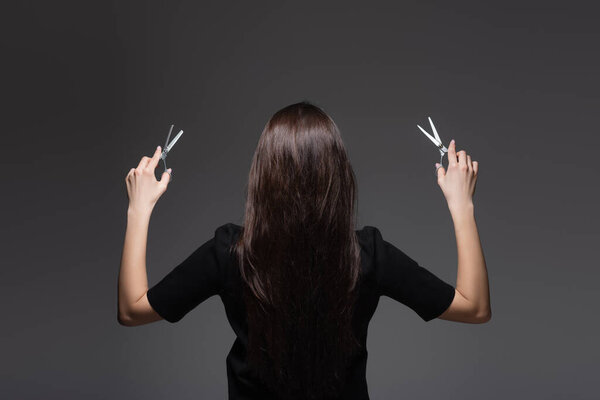 back view of young woman with long shiny hair holding scissors isolated on dark grey