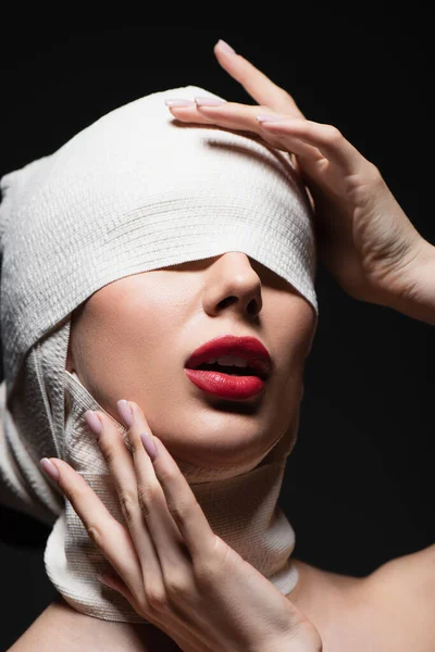 woman in elastic bandage with covered eyes and opened mouth isolated on dark grey