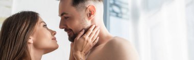 happy woman looking at boyfriend and touching his face in bedroom, banner