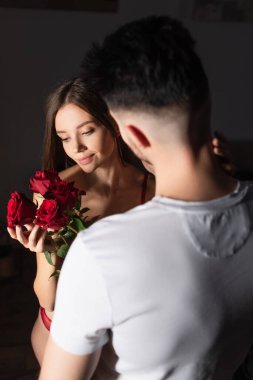 back view of blurred man in white t-shirt presenting red roses to sensual smiling woman