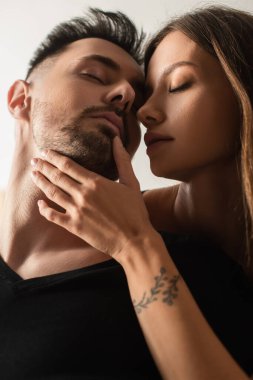 sensual woman with closed eyes touching face of man isolated on white