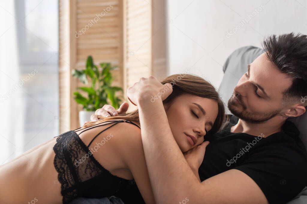 young man hugging sexy woman in lace bra lying on his chest with closed eyes