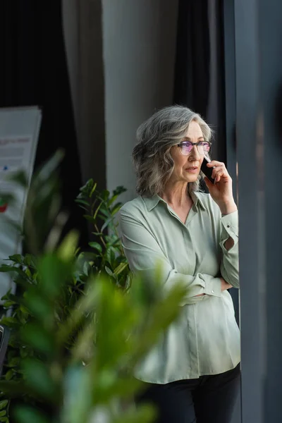 Mature Businesswoman Talking Mobile Phone Blurred Plants Office — Stock Photo, Image