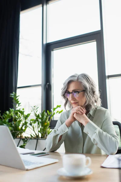 Rijpere Zakenvrouw Zoek Naar Laptop Buurt Wazig Kopje Koffie Het — Stockfoto