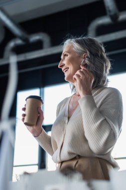 Ofiste elinde kağıt bardakla gülümseyen iş kadınının düşük açılı görüntüsü. 