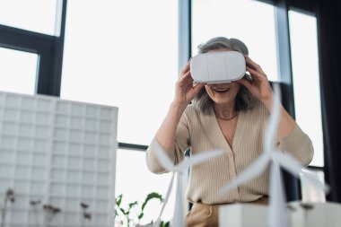 Ofisteki binaların modellerinin yanında vr kulaklık takan olgun bir iş kadını. 