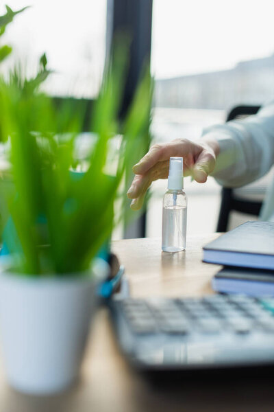 Обрезанный взгляд на деловую женщину, принимающую дезинфицирующее средство для рук на столе в офисе 